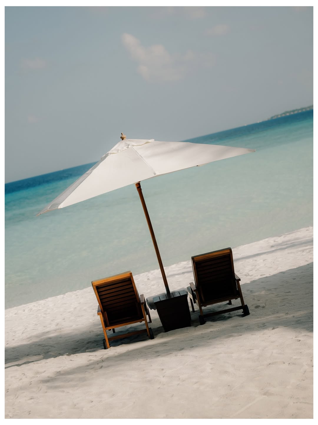 Two loungers and a white parasol on white sand by a turquoise sea